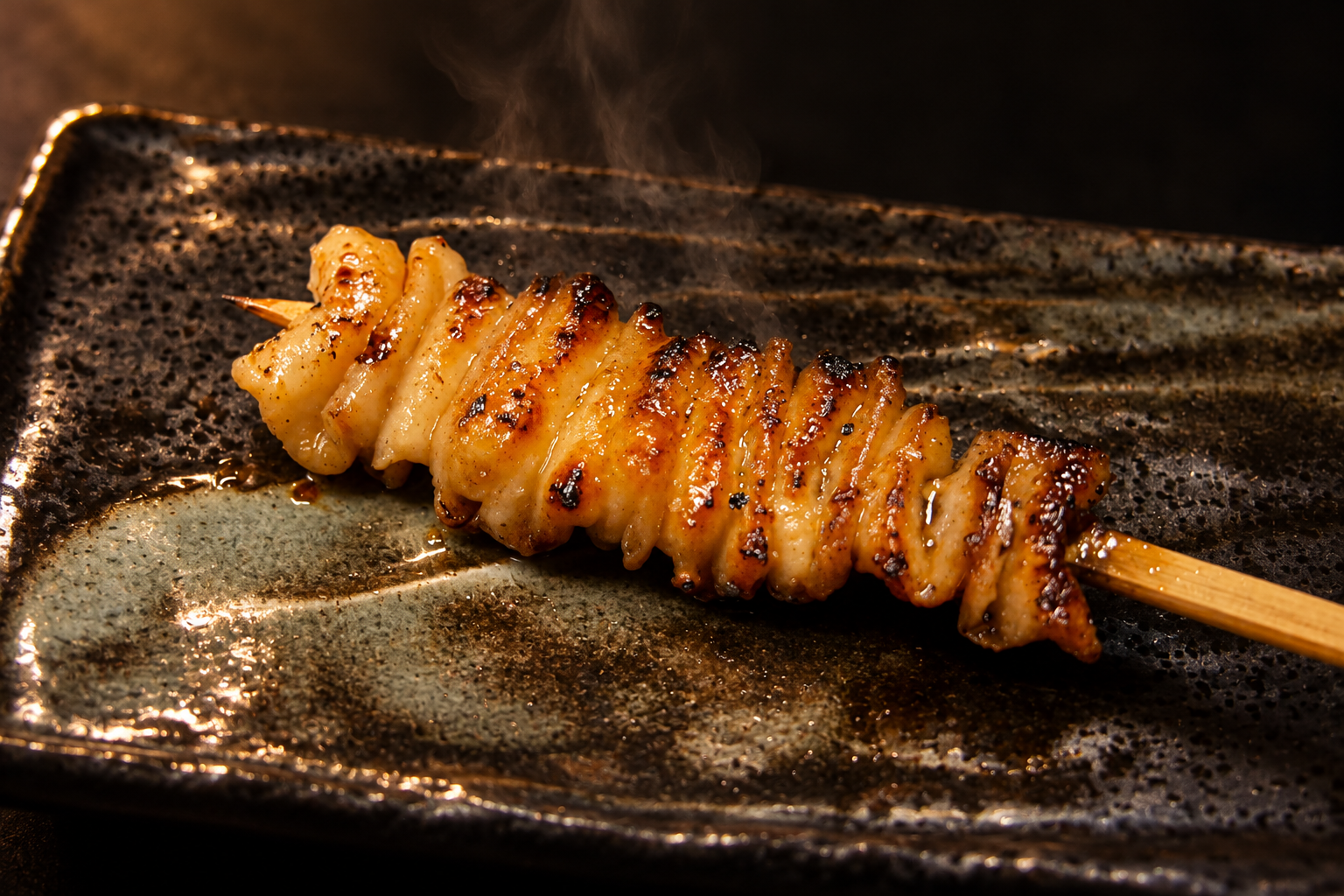 A single chicken skewer, its pieces threaded evenly, on a dark plate at Yakitori Senkichi