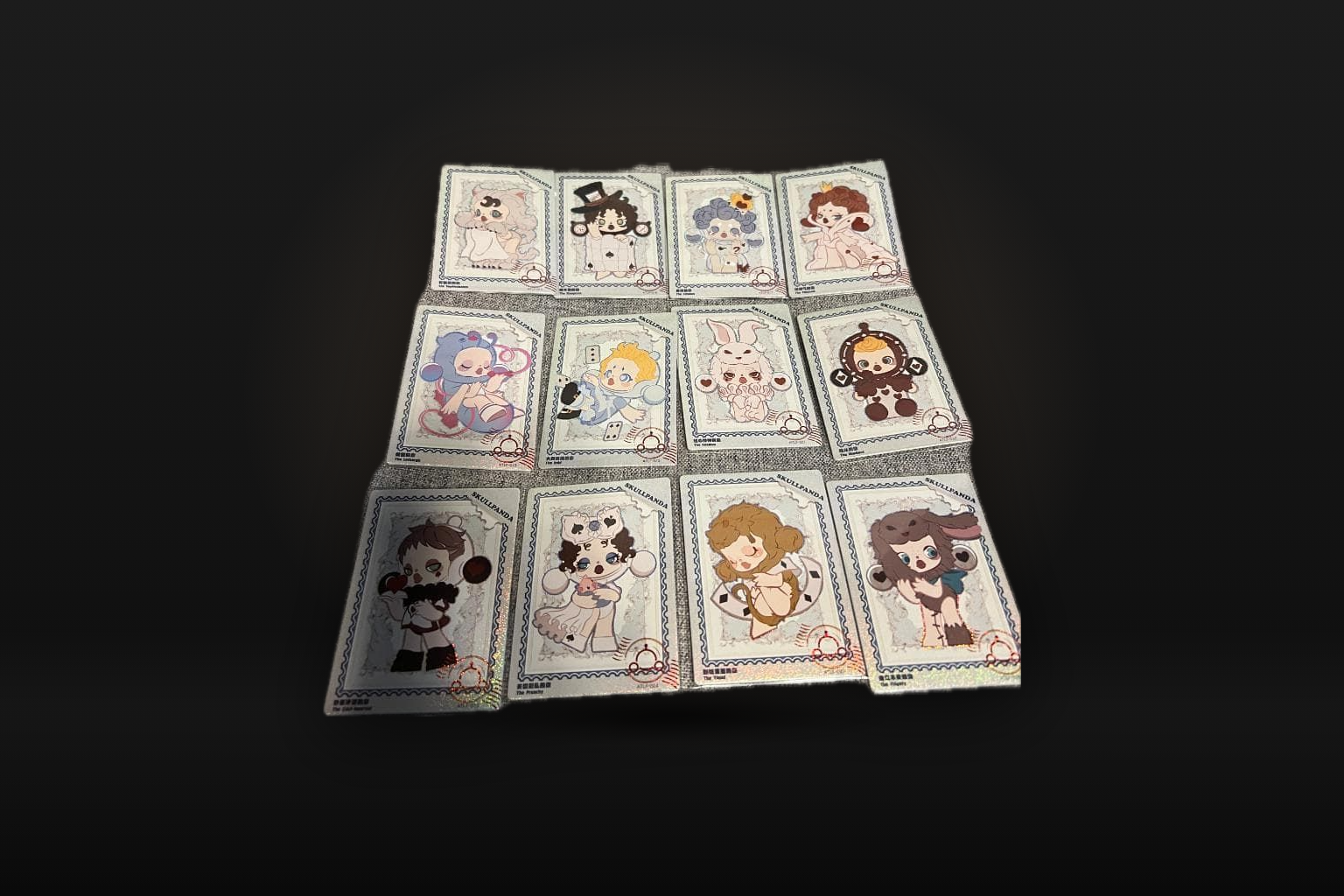 Thirteen SKULLPANDA art cards in sleeves laid out on a dark background, one above three rows of four