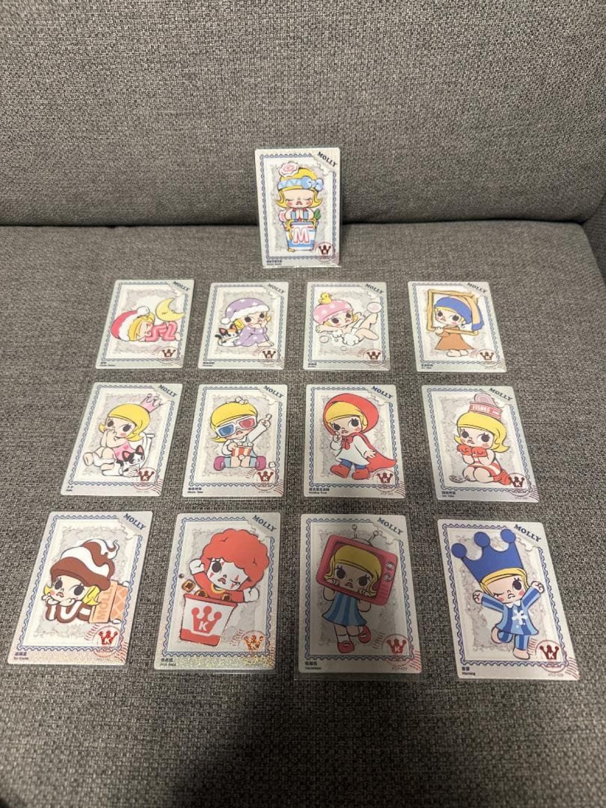 Thirteen sleeved MOLLY art cards laid out on a grey sofa