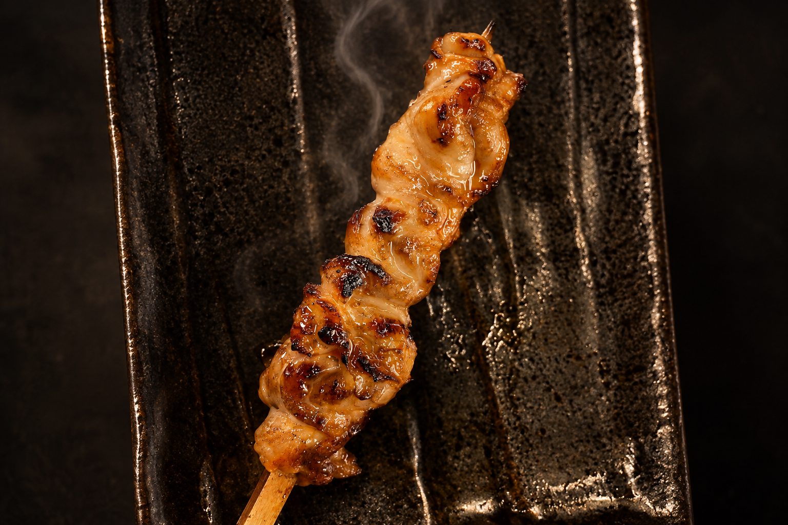 黒い長皿にのった、焼き目のついた肉の串。湯気が立っている