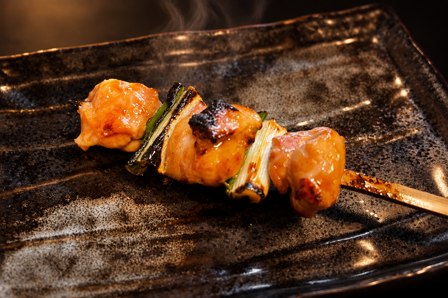 暗い器にのった、鶏肉とねぎを交互に刺した焼鳥（ねぎま）の串