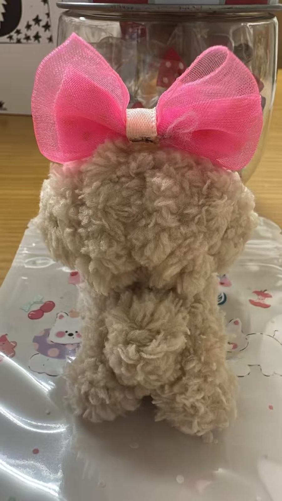 The beige fluffy dog doll seen from behind, with the pink bow on its head