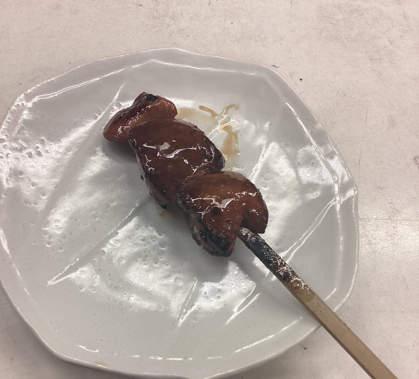 A chicken liver skewer grilled with tare on a white plate