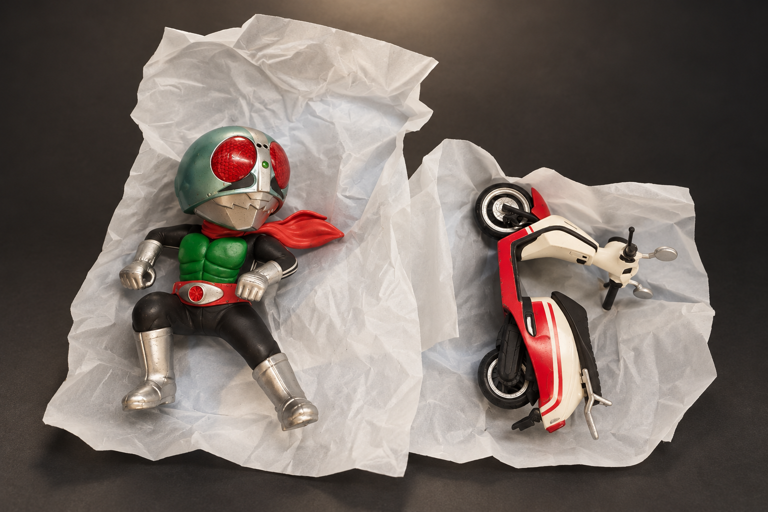 深いグレーの背景に置いた、仮面ライダー1号のデフォルメフィギュアと赤白のスクーター型バイク
