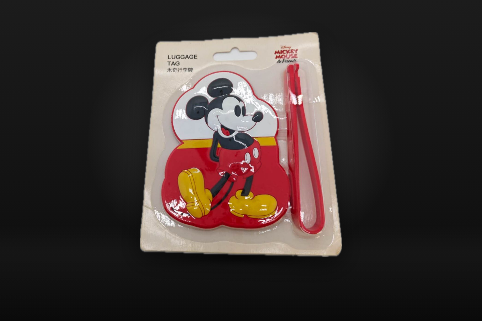 黒い背景に置かれた、台紙付きのミッキーマウスのラゲッジタグ。赤いベルトが付き、台紙に「LUGGAGE TAG 米奇行李牌」とある