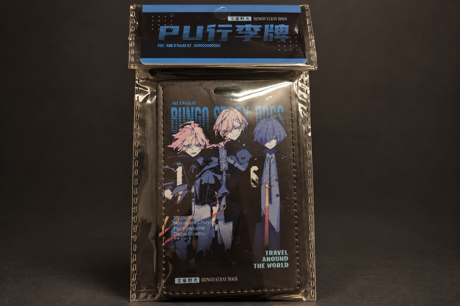 A Bungo Stray Dogs luggage tag in its clear package with a header reading PU行李牌 and SHANGHAI, showing three characters and the words TRAVEL AROUND THE WORLD, on a dark grey background