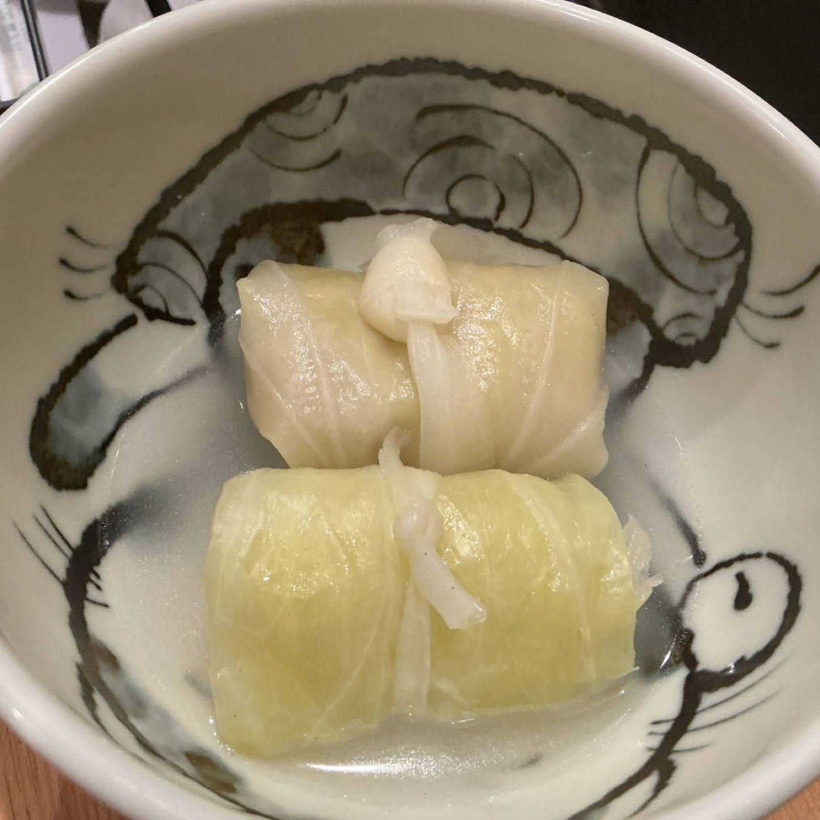 Two cabbage rolls tied with kanpyo in a white bowl with an ink-brush pattern (unedited photo)