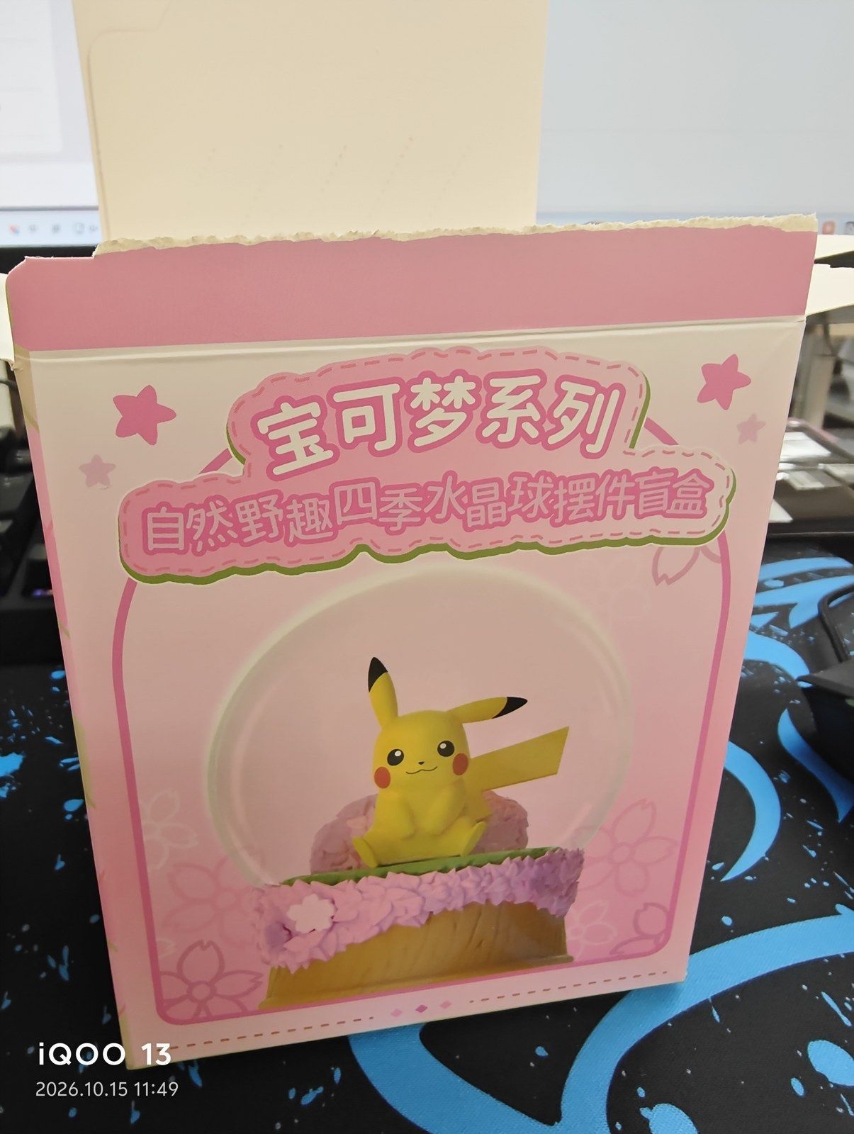 The front of a pink box printed with 宝可梦系列 and 自然野趣四季水晶球摆件盲盒 and a picture of the Pikachu snow globe on a pink base; the top of the box has been opened (unedited photo; the camera's date stamp is visible at bottom left)