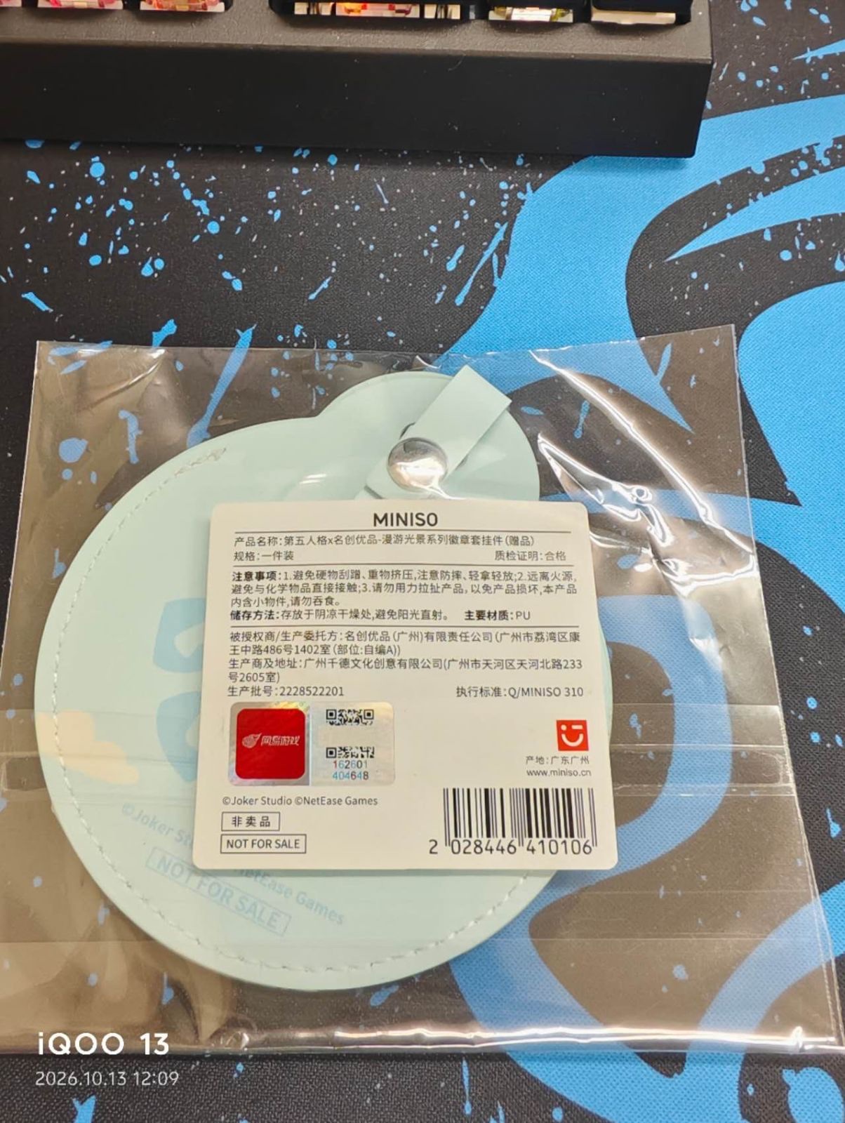 透明な袋に入った缶バッジカバーの裏側。スナップボタン付きのストラップと、中国語で品名や注意事項が書かれた白いMINISOのラベル、赤い「网易游戏」のシール、「非卖品 NOT FOR SALE」の表示が見える（未加工の写真、左下にカメラの撮影日時表示あり）