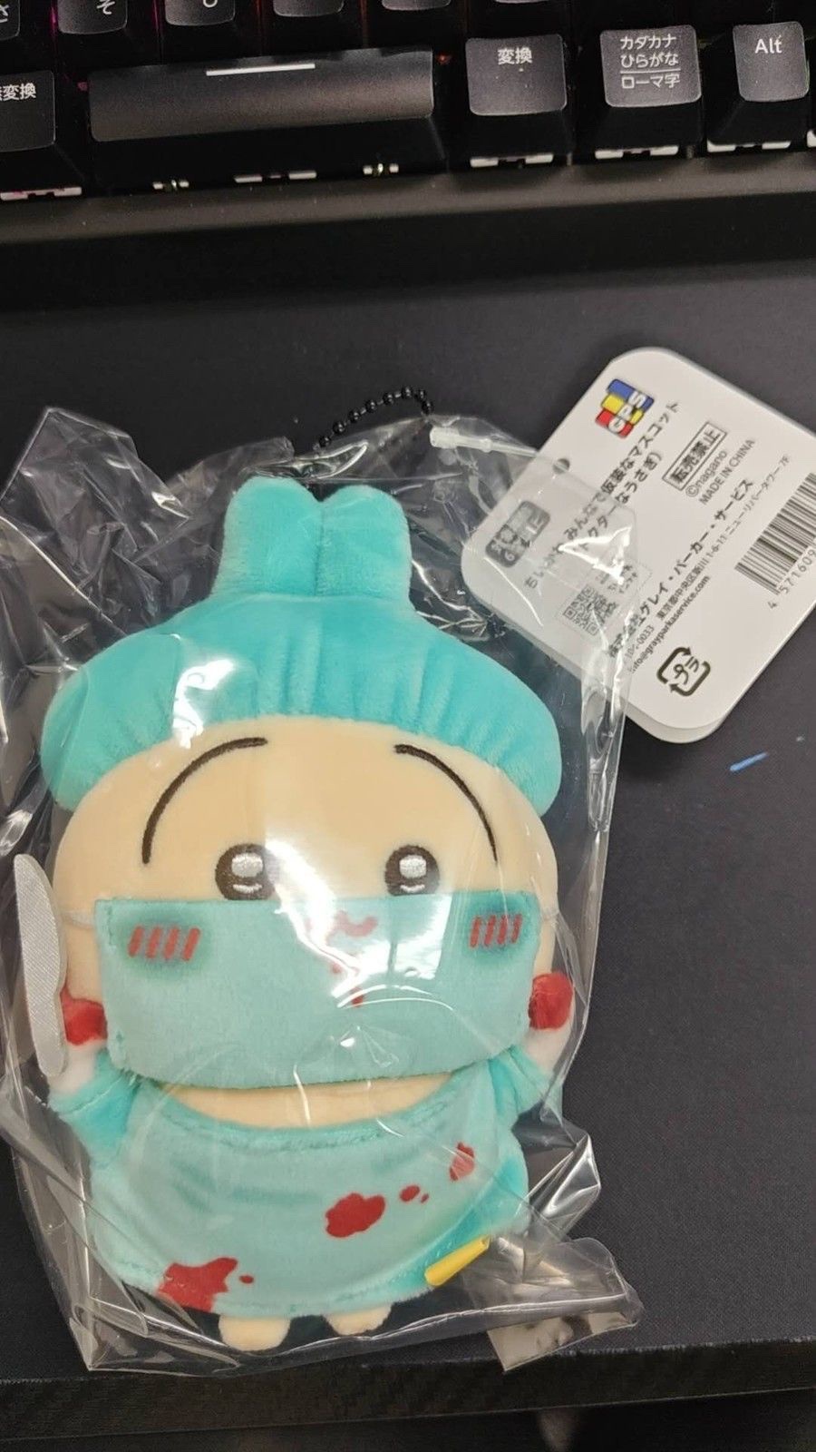 Doctor Usagi mascot in a clear bag on a black mat, in a mint-green surgical cap, mask and gown, with the header tag and ball chain at the top right (unedited photo; a keyboard is visible at the top)