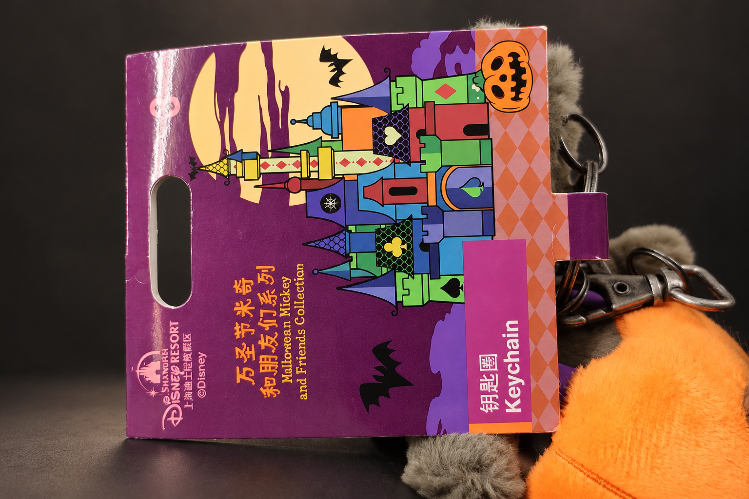 A purple Chinese header tag reading "Halloween Mickey and Friends Collection" and "Keychain", attached to a grey plush with a metal clasp, against a dark background