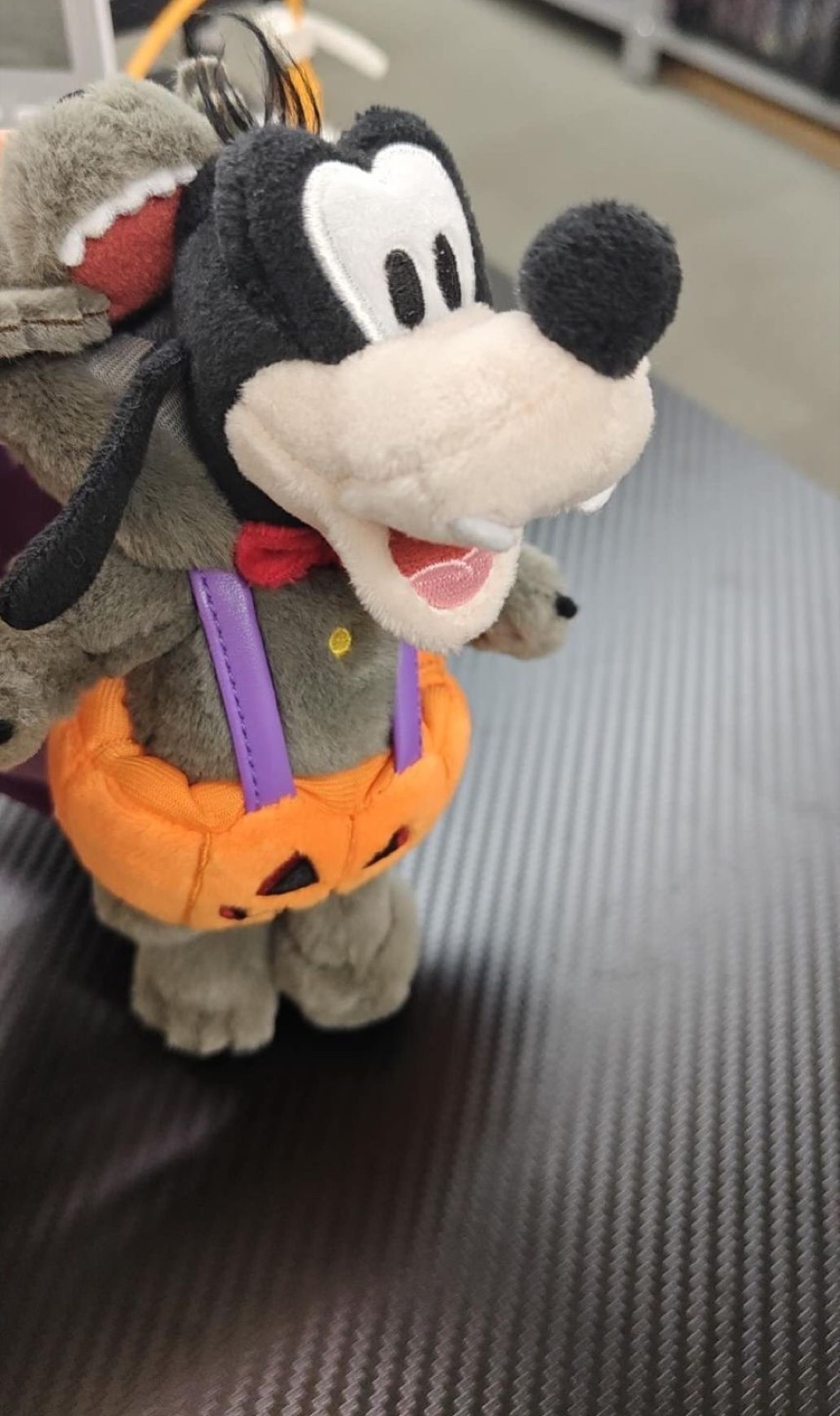 灰色のオオカミ風フードをかぶり、紫のサスペンダー付きのかぼちゃパンツをはいたグーフィーのぬいぐるみ。口元に白い牙がある