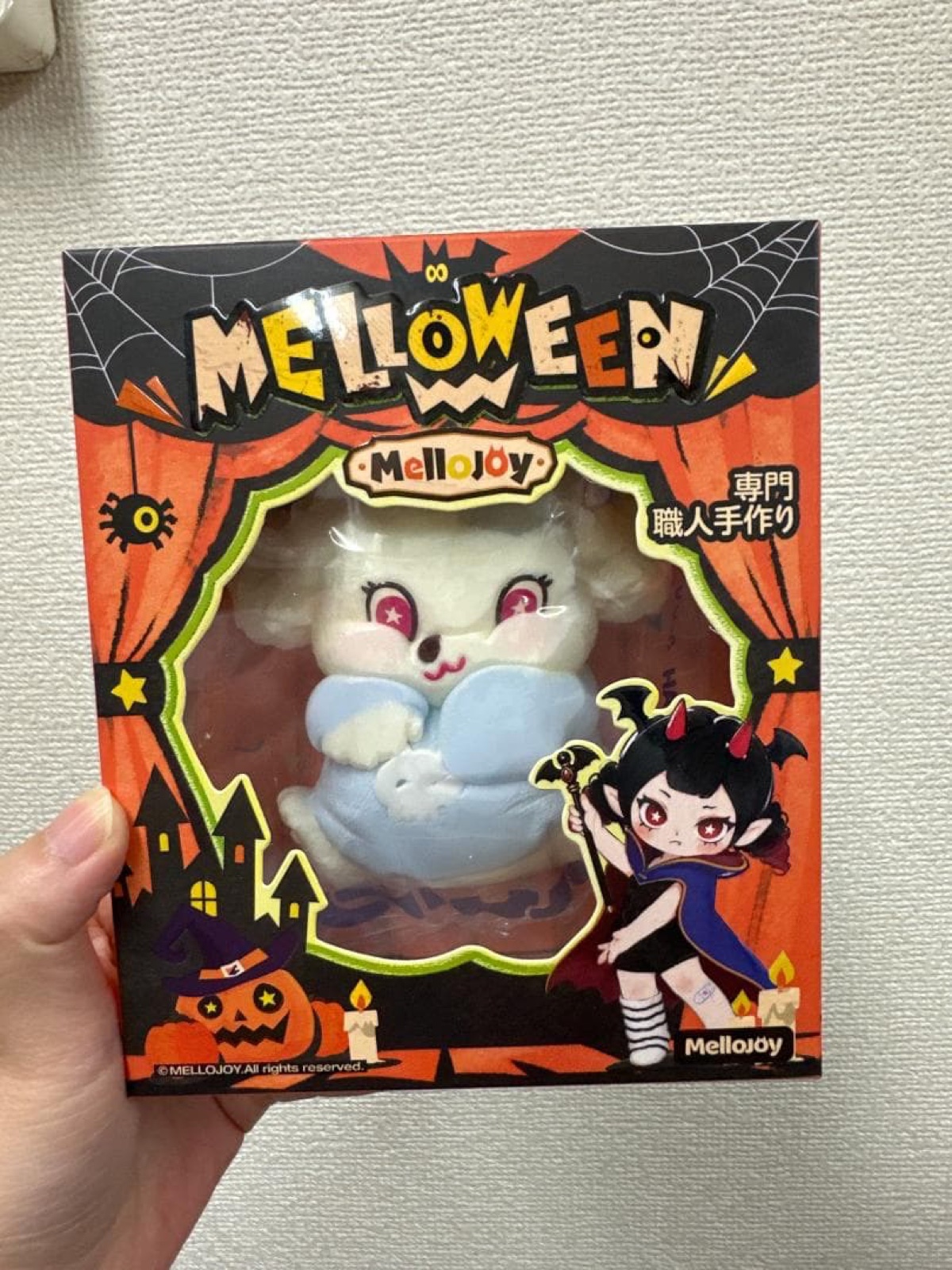 オレンジ色のMELLOWEENの箱の表面。透明な窓からスクイーズ本体が見え、ハロウィンのイラストと「専門職人手作り」の文字がある