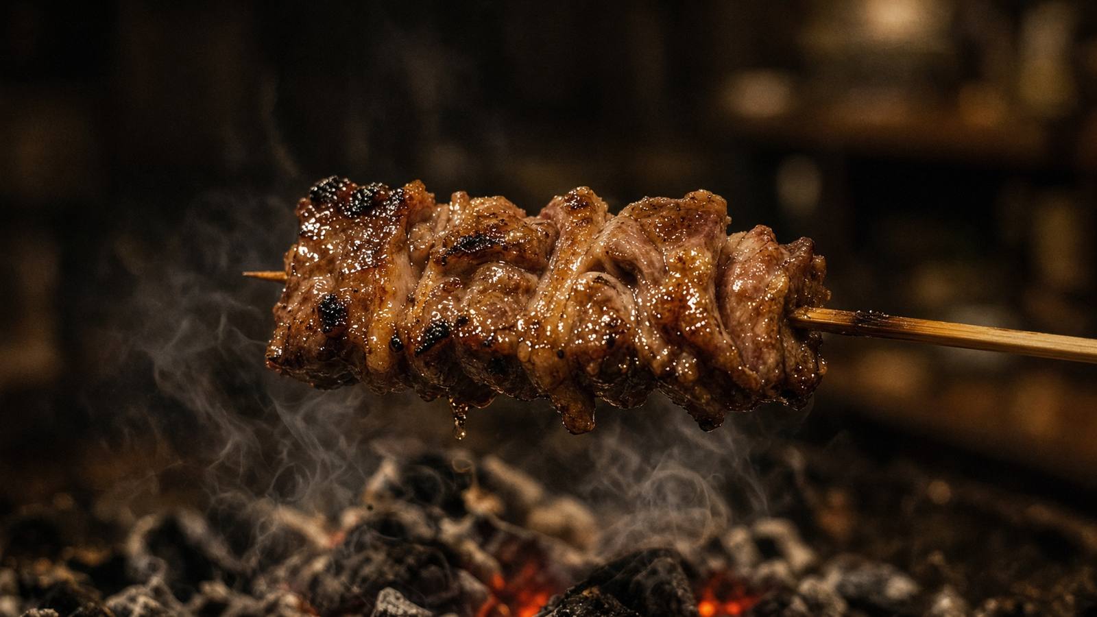 A grilled meat skewer held above charcoal in a dark setting