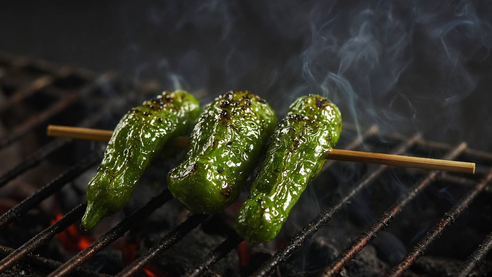 炭火の上で焼かれる緑色のししとう串のイメージ