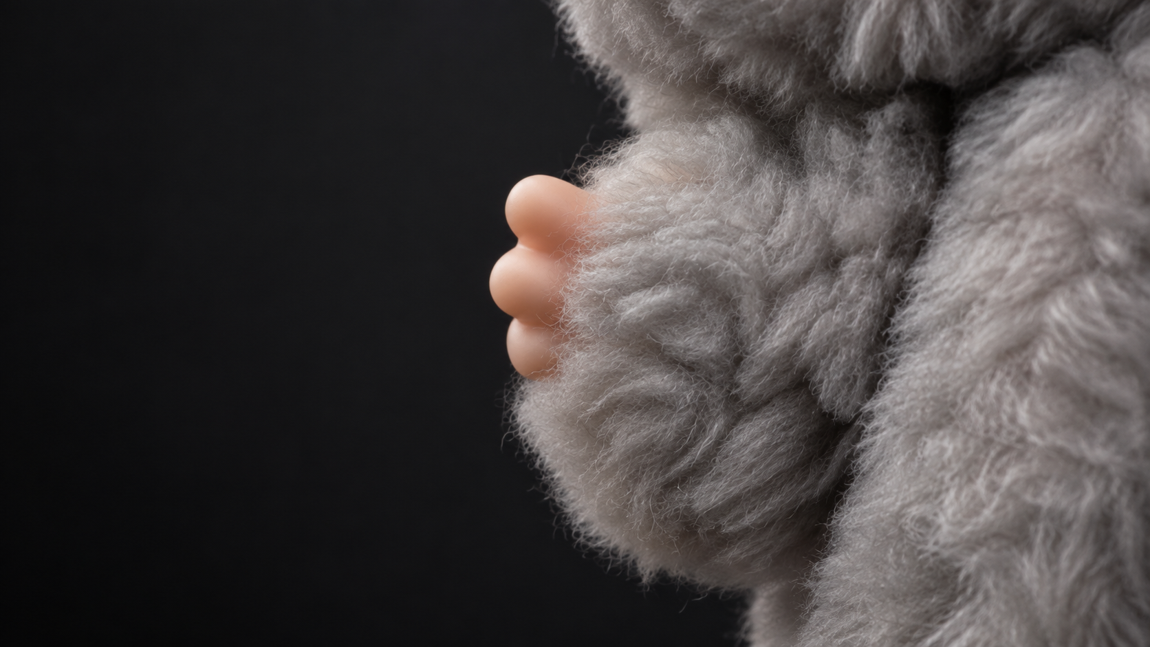 Edited close-up based on the listing photo, showing grey plush texture and a small vinyl hand against charcoal grey