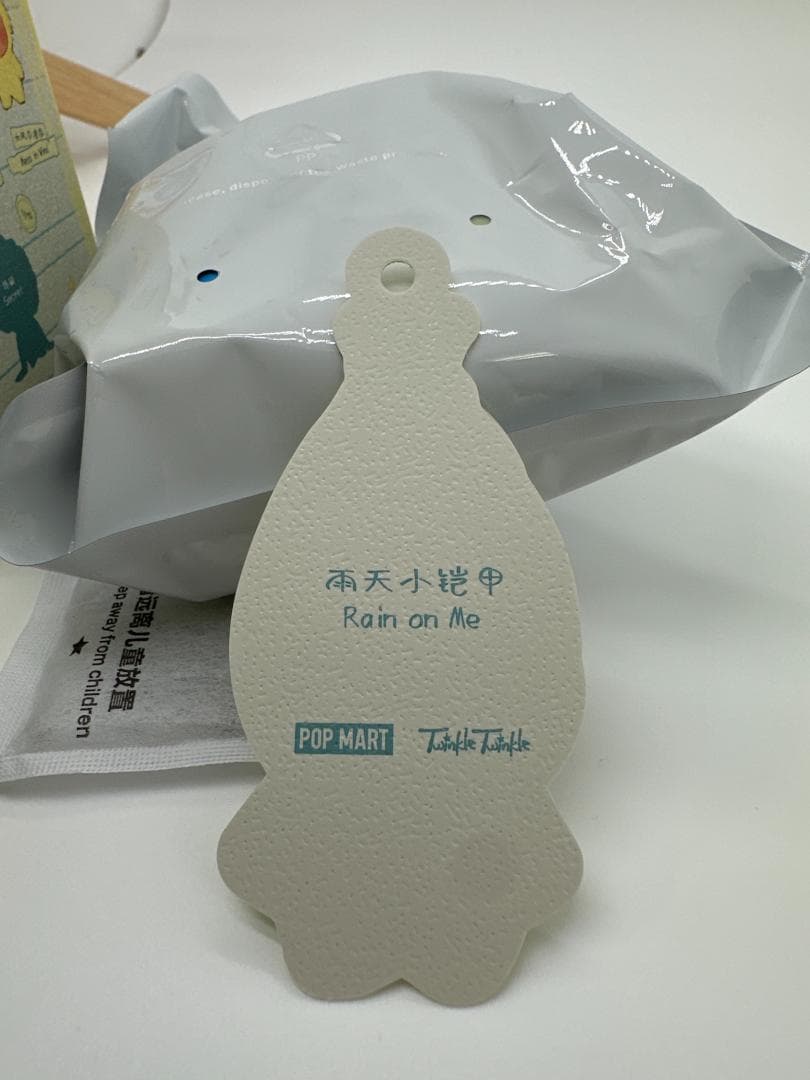 Unedited listing photo showing Rain on Me printed on the reverse of the character card beside the inner bag